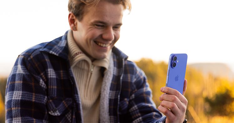 gutt som holder iphone 16 og smiler
