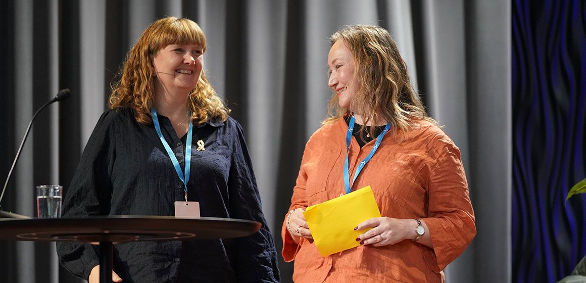 To personer med blå ID-bånd på en scene under konferanse