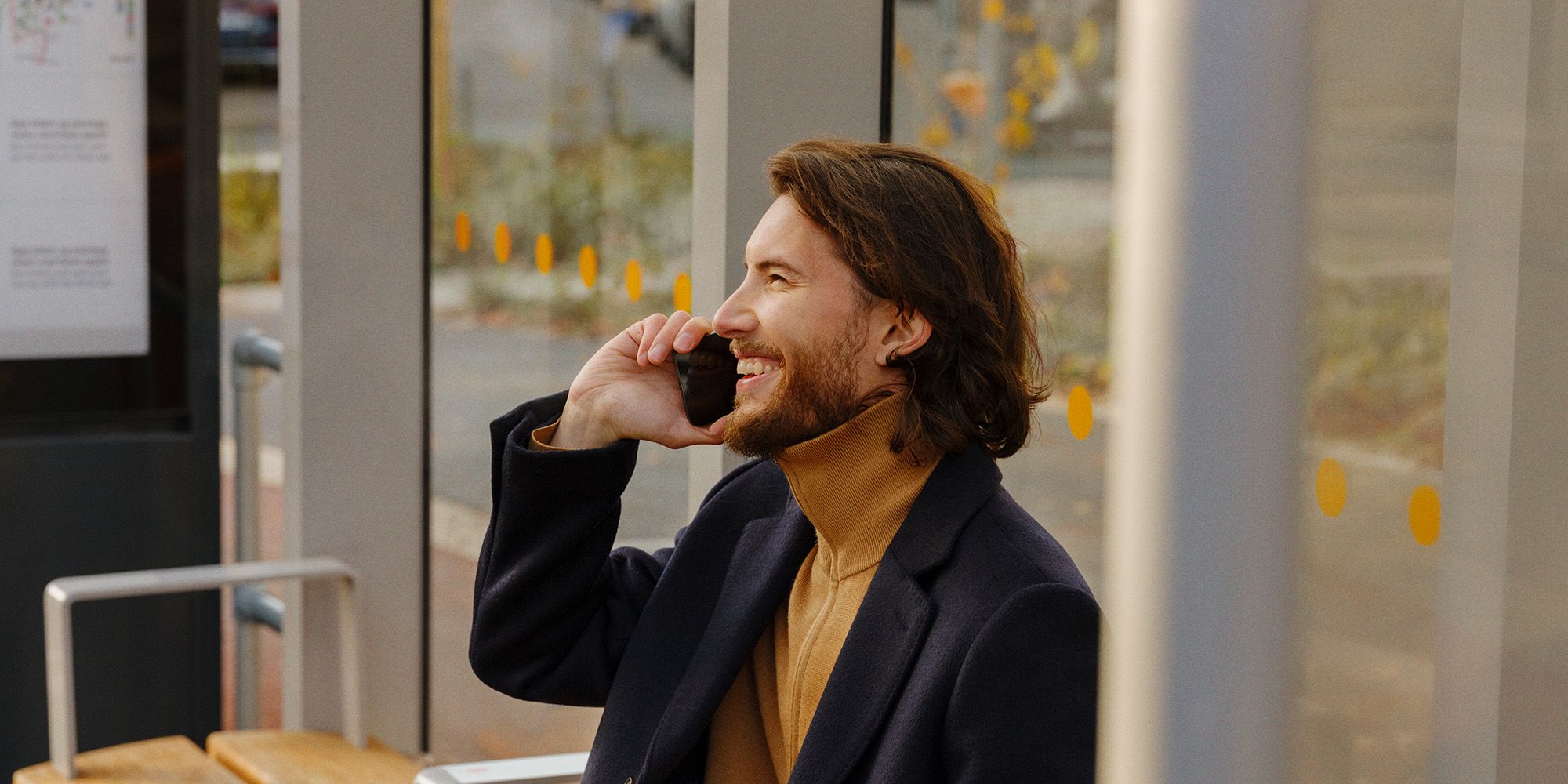 En mann som sitter på bussholdeplassen og snakker i mobilen