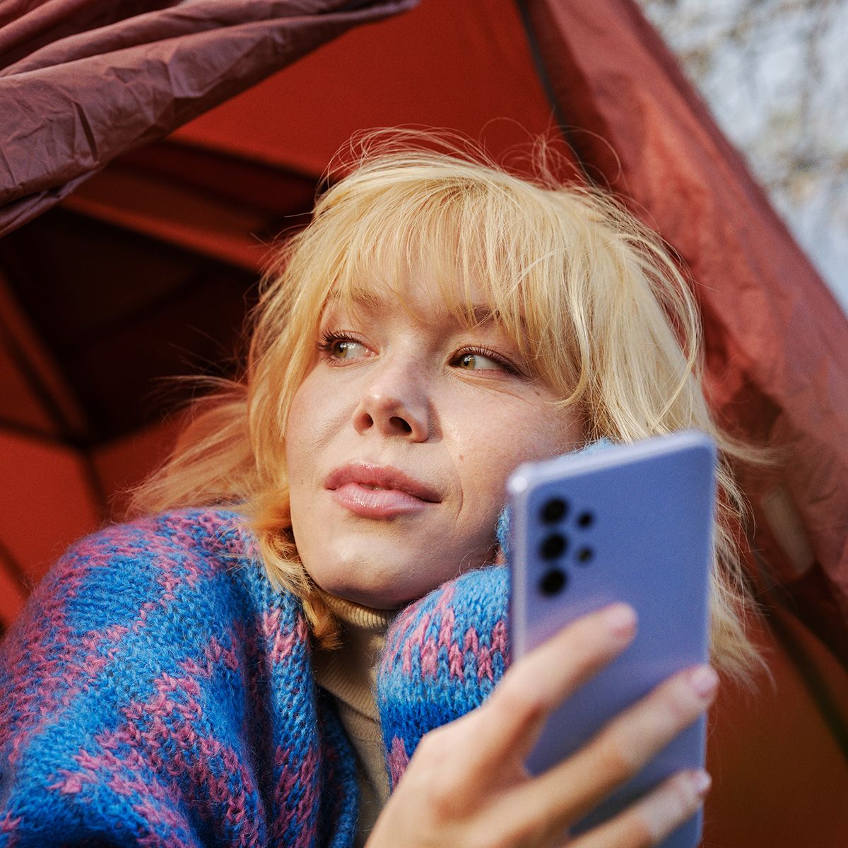 en jente på telttur kikker ut av teltet med mobilen i hånda