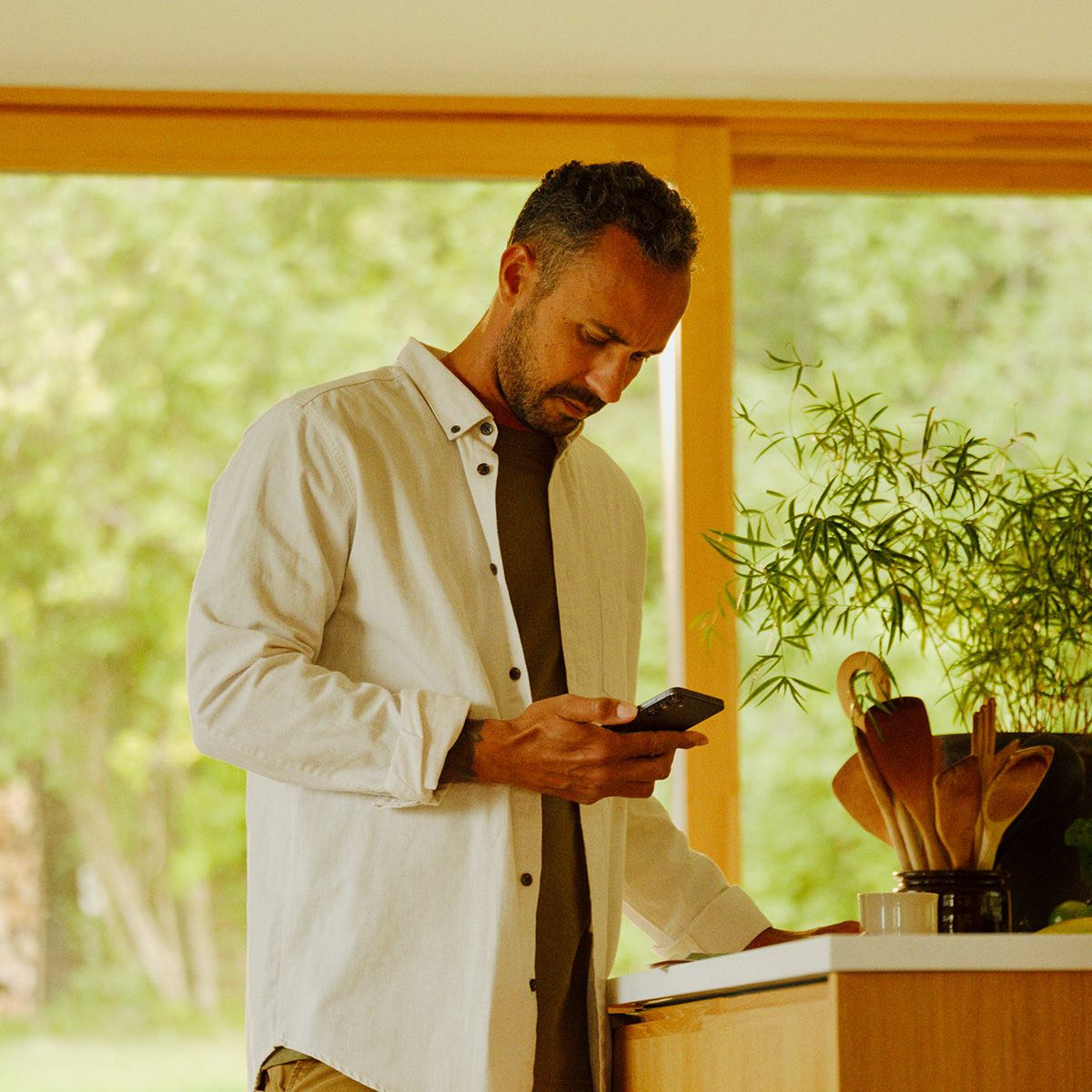 en mann som står ved kjøkkenbenken og ser ned på mobilen sin