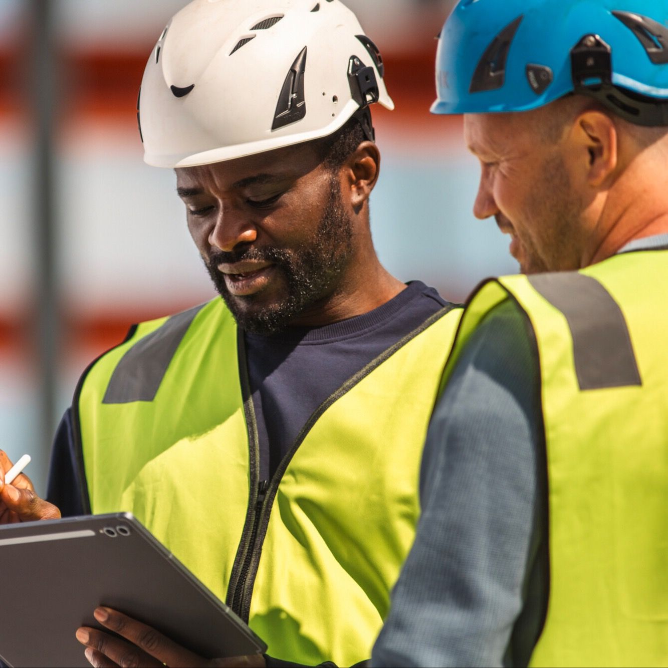 Bilde av to personer som jobber på byggeplass. Den ene holder et nettbrett i hånden.
