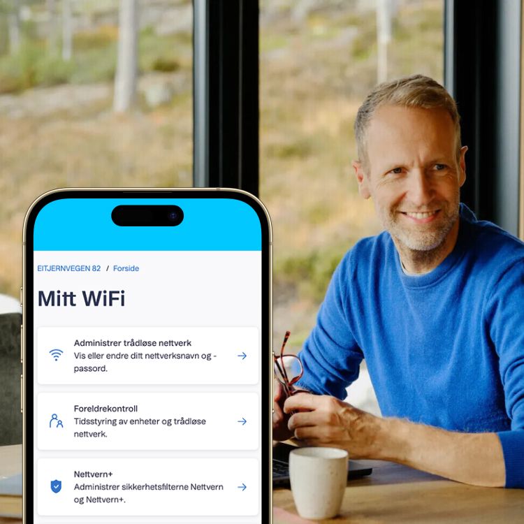 Mobiltelefon som viser Mitt WiFi-appen, med en smilende mann ved en bærbar PC i bakgrunnen.