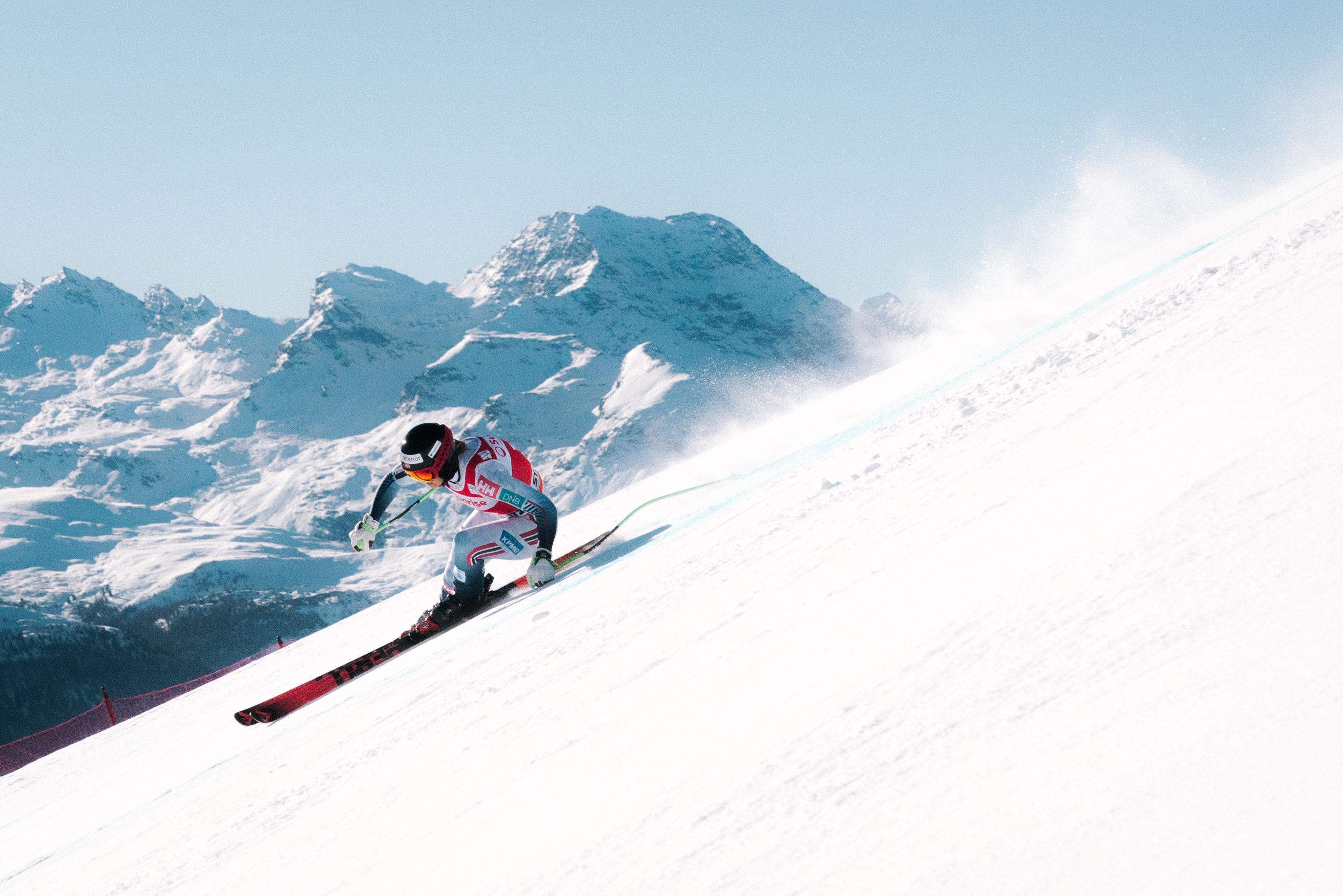 En alpinist i full fart nedover en snødekt fjellside med høye fjell i bakgrunnen