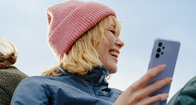 en jente med rosa lue ler mens hun holder mobilen sin i hånda