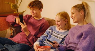 Familie ser TV og surfer med telefon.