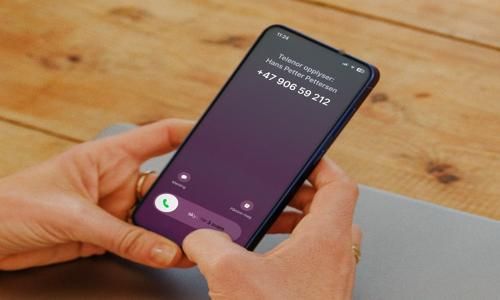 en mann med en rosa lue og en blå skjorte sitter på cafe og ser på mobilen
