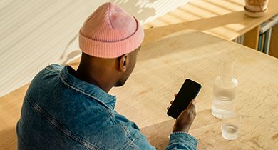 en mann med en rosa lue og en blå skjorte sitter på cafe og ser på mobilen