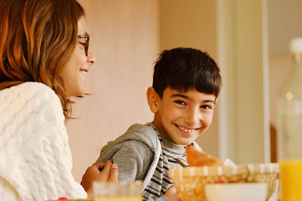 en gutt som sitter ved frokostbordet med søsteren sin og smiler til kameraet