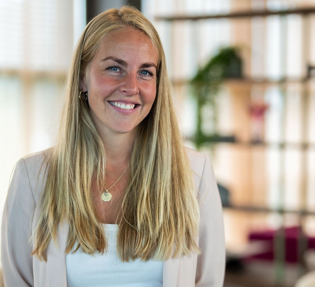 Kvinne i beige dressjakke og bukse foran moderne kontorinteriør