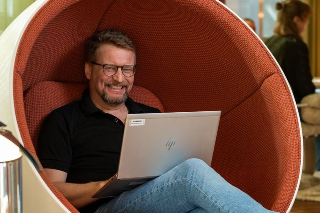 Person sitter i en rund stol med en bærbar PC og hvite joggesko