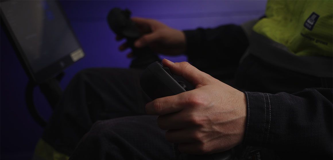 Hender som kontrollerer joystick med skjerm i bakgrunnen