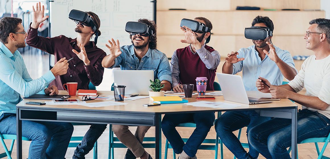 Personer tester VR-briller rundt et bord på en arbeidsplass