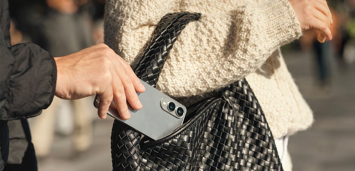 En hånd som stjeler en mobil fra en kvinnes veske
