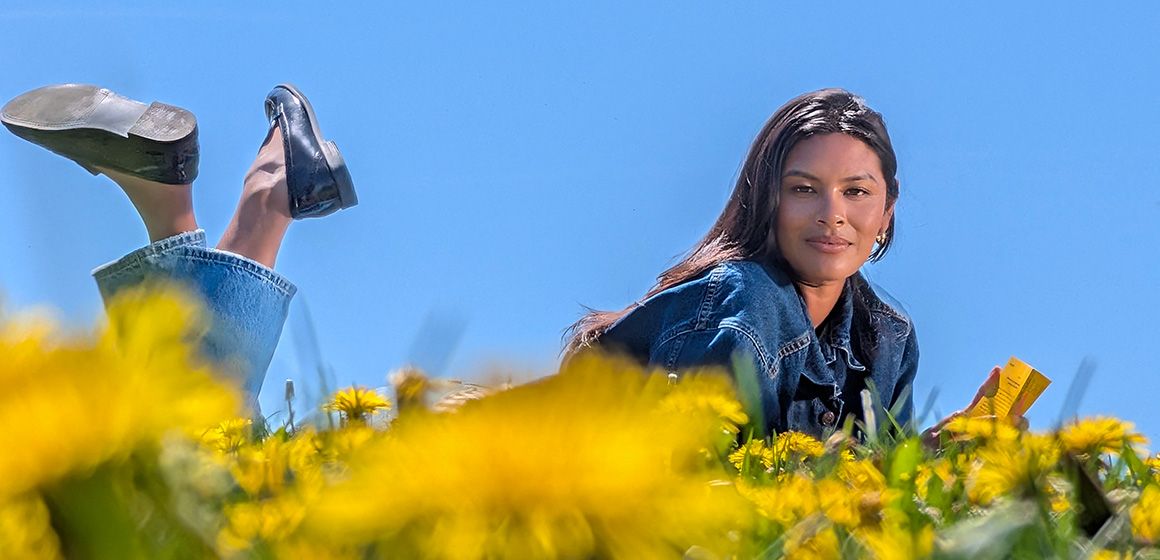 Nærbilde av damen som ligger i den gule blomsterengen med blå himmel i bakgrunnen