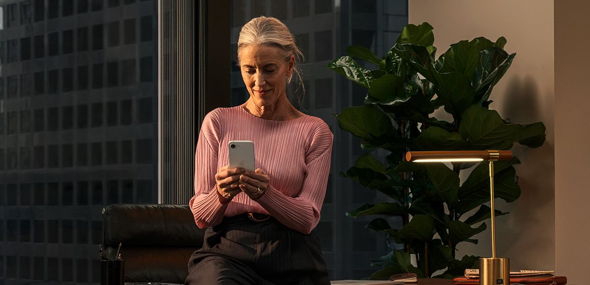 en dame med en rosa genser ser på sin iphone 17e på kontoret