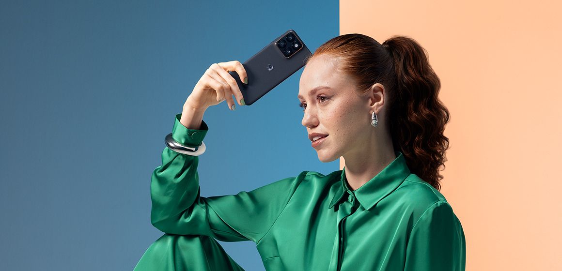 en dame med rødt hår og grønn silkeskjorte holder en motorola edge 70 fusion i hånden