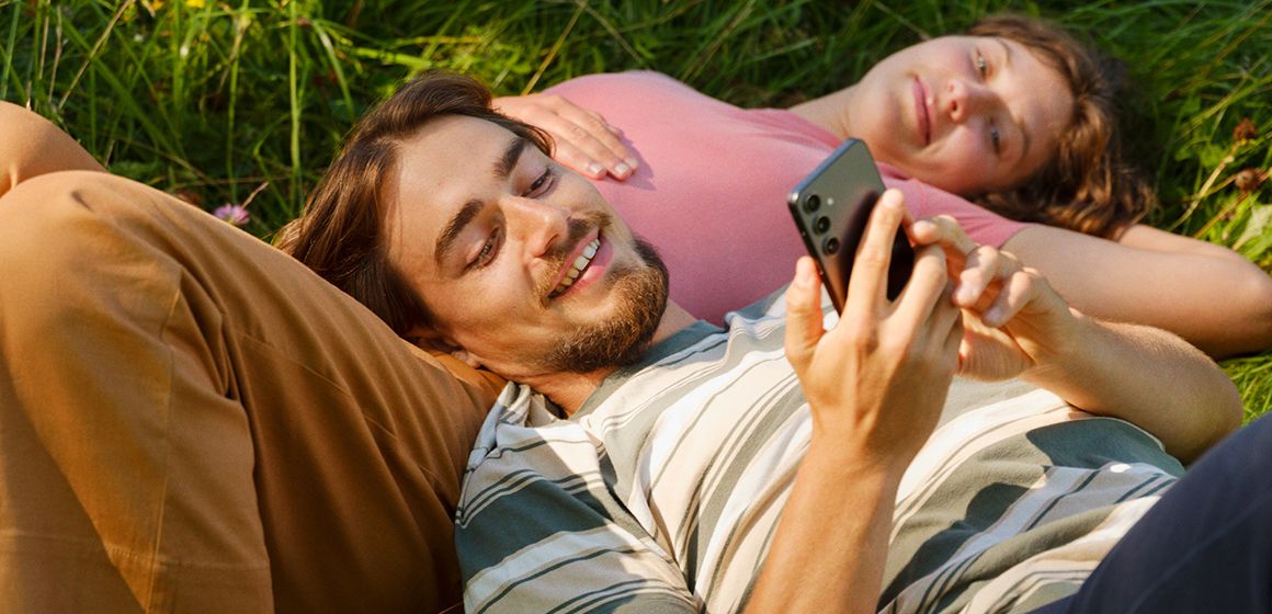 en mann og en dame som ligger i gresset og ser på mobiltelefonen