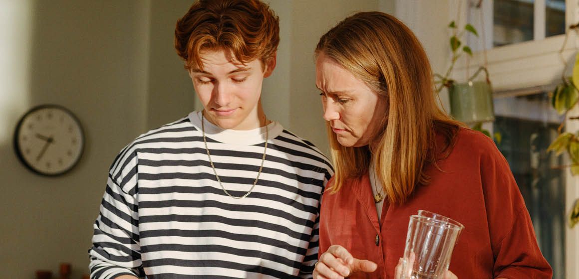 Mor og sønn som ser ned på mobil etter at de har blitt svindlet.