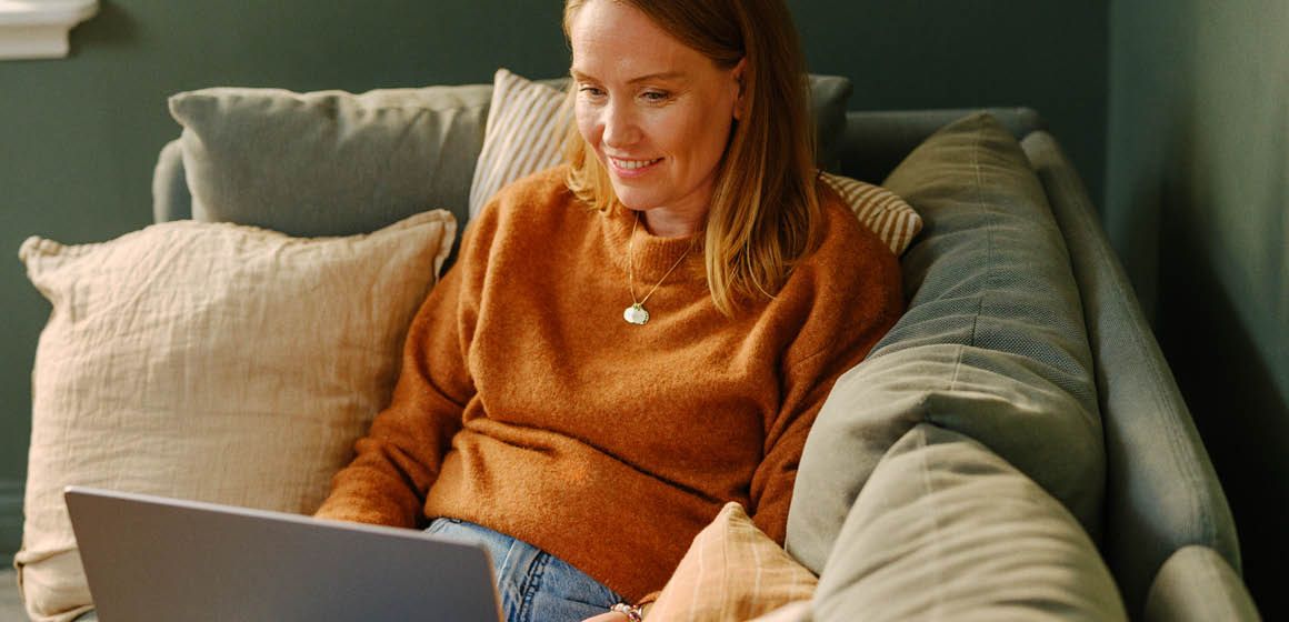 Person i oransje genser sitter på en sofa med en laptop