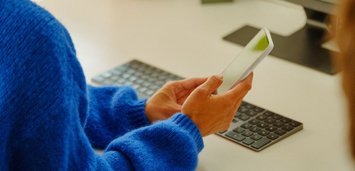 en dame med blå genser sitter og scroller på mobilen sin