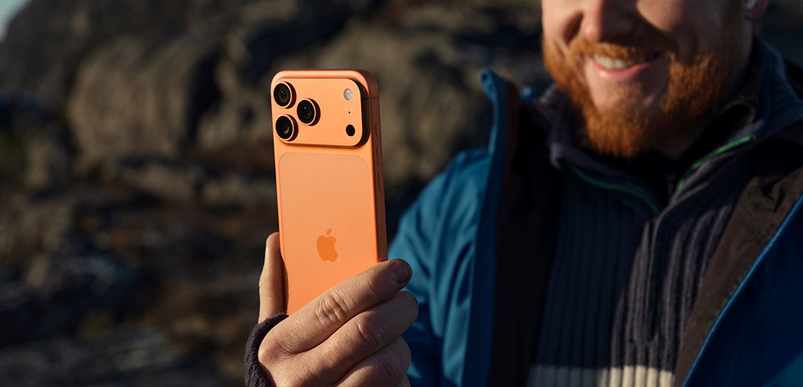 en mann som holder en iphone 17 pro max i fargen kosmisk oransje og smiler