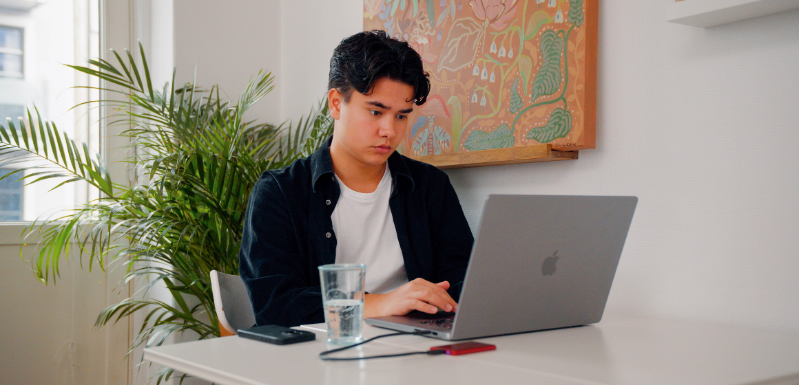 Person foran Macbook, plante og kunst på vegg