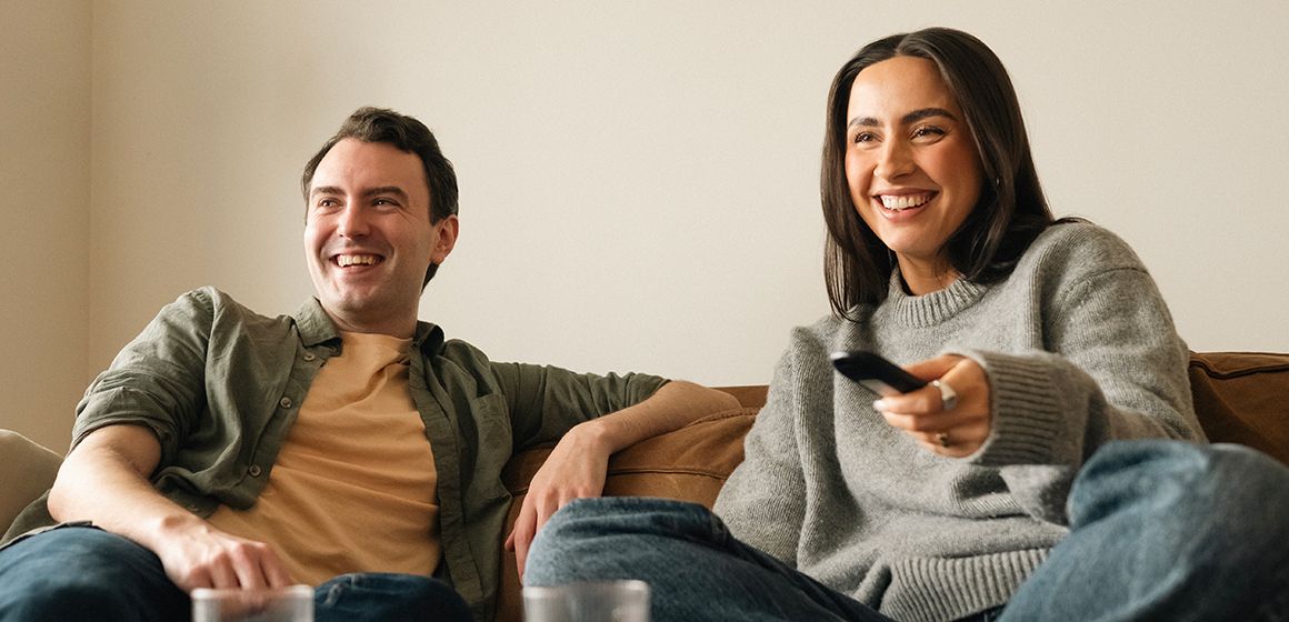 To personer sitter i stuen, én holder en fjernkontroll til t-we boks III.