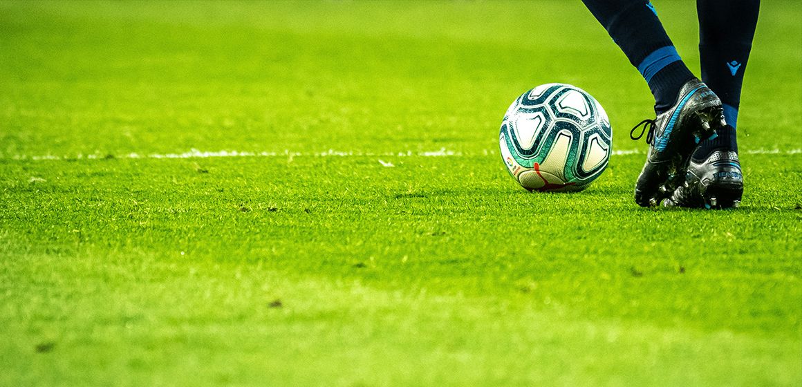 Fotballspiller med ball på grønn gressbane, som er blant sport i t-we.