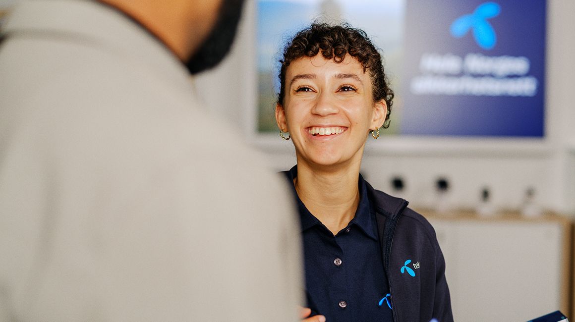 en jente som jobber i telenorbutikken smiler mens hun hjelper en kunde