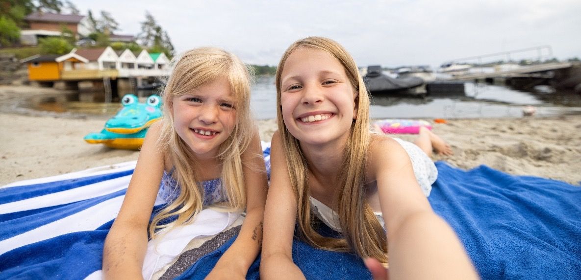 Sommerminne: to søstre som tar selfie mens de ligger på et badehåndkle på stranda
