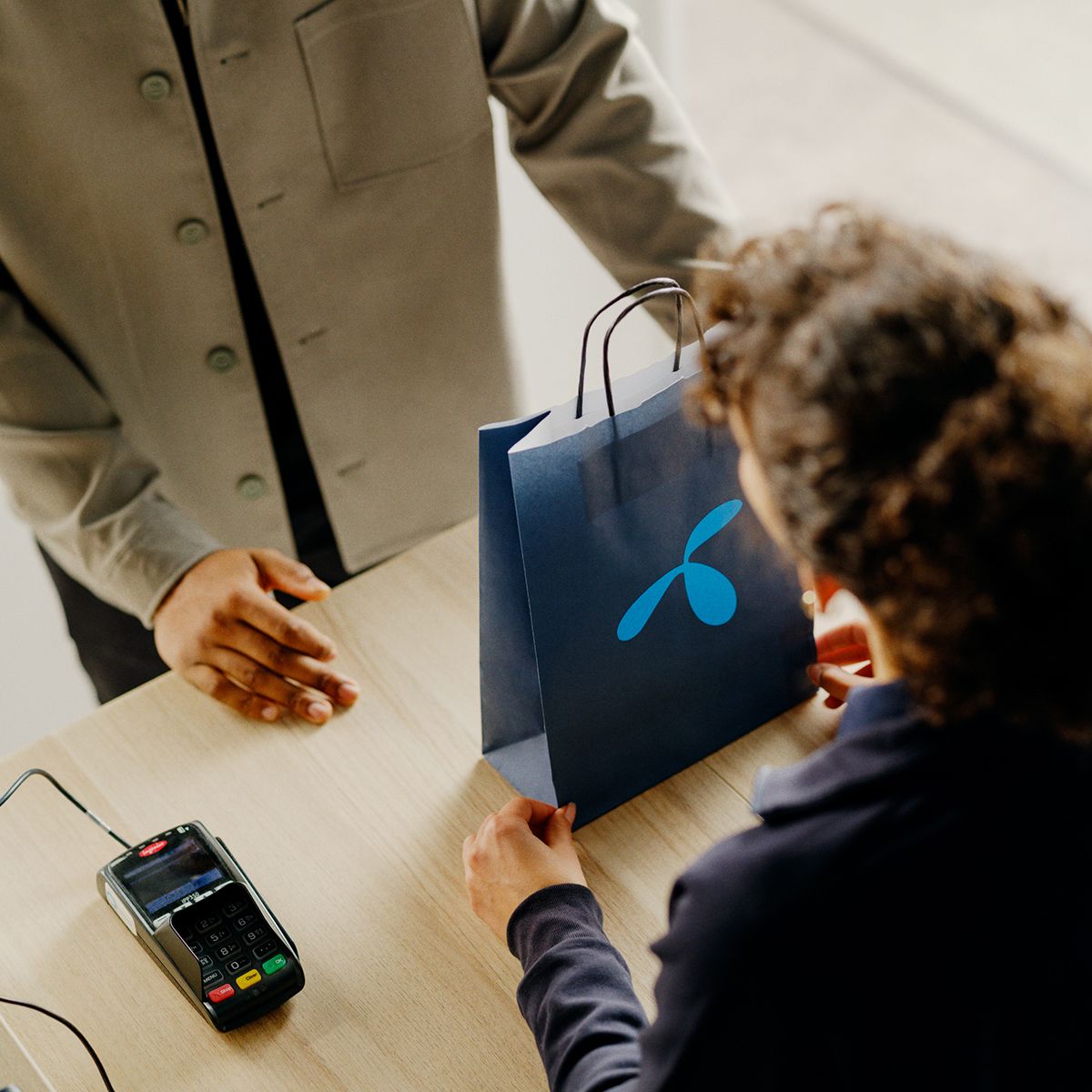 Person mottar en blå handlepose ved en betalingsterminal