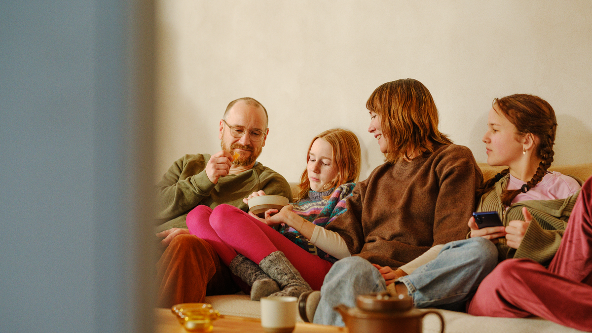 En familie på fire sitter i sofaen, spiser snacks og ser på TV.