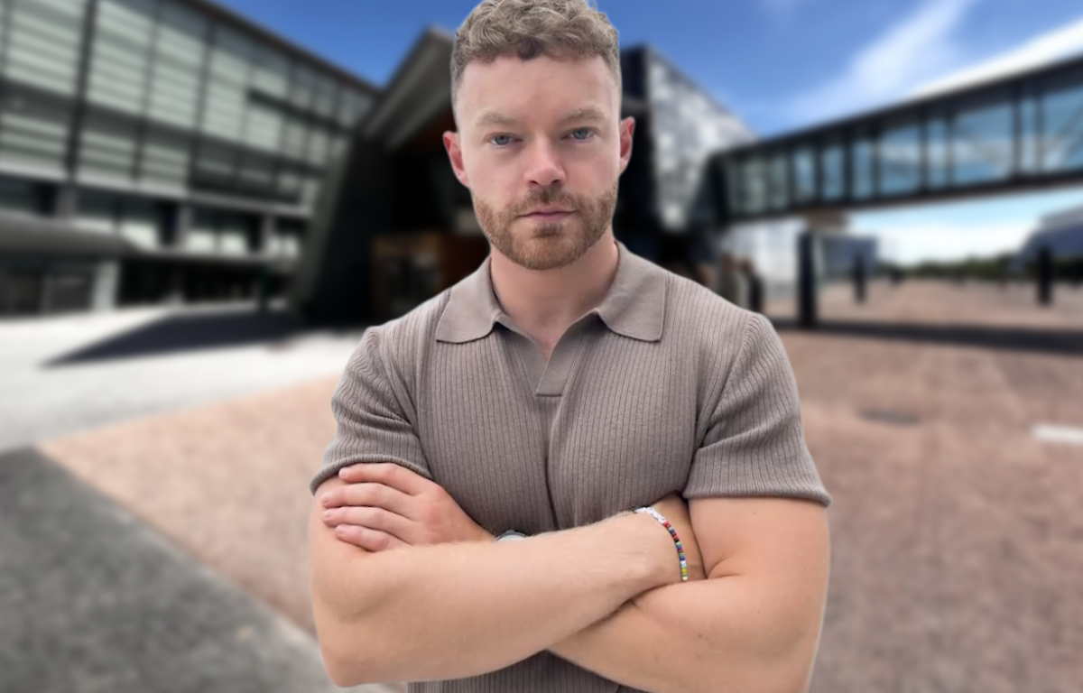 Person med armene krysset foran moderne bygning under blå himmel