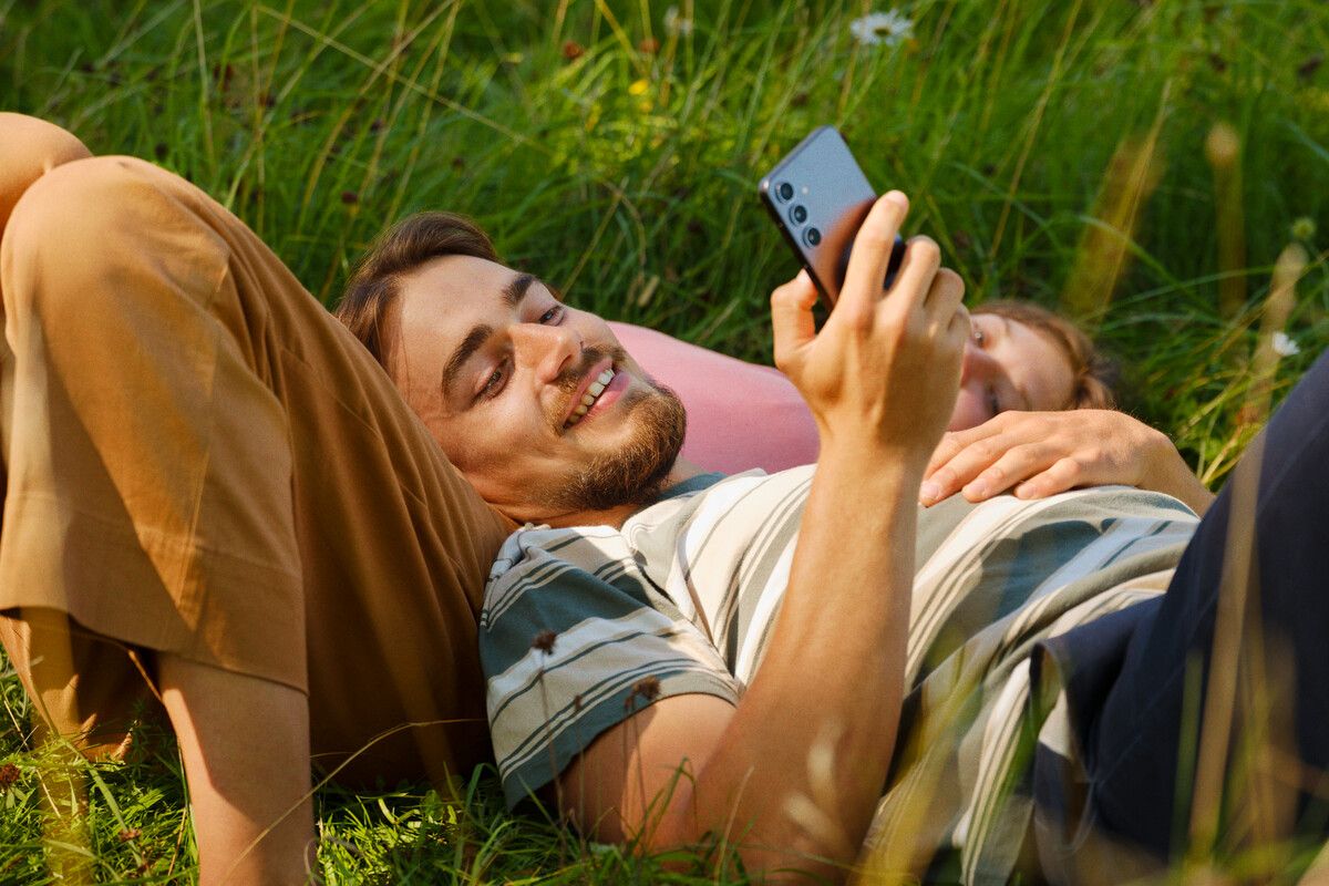 to som ligger i gresset og ser på mobilen