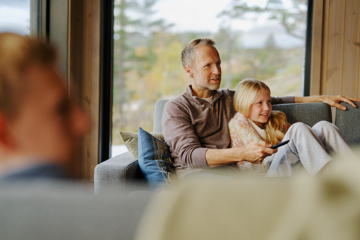 En mann og en jente sitter i en sofa og ser på TV. Mannen holder en fjernkontroll.