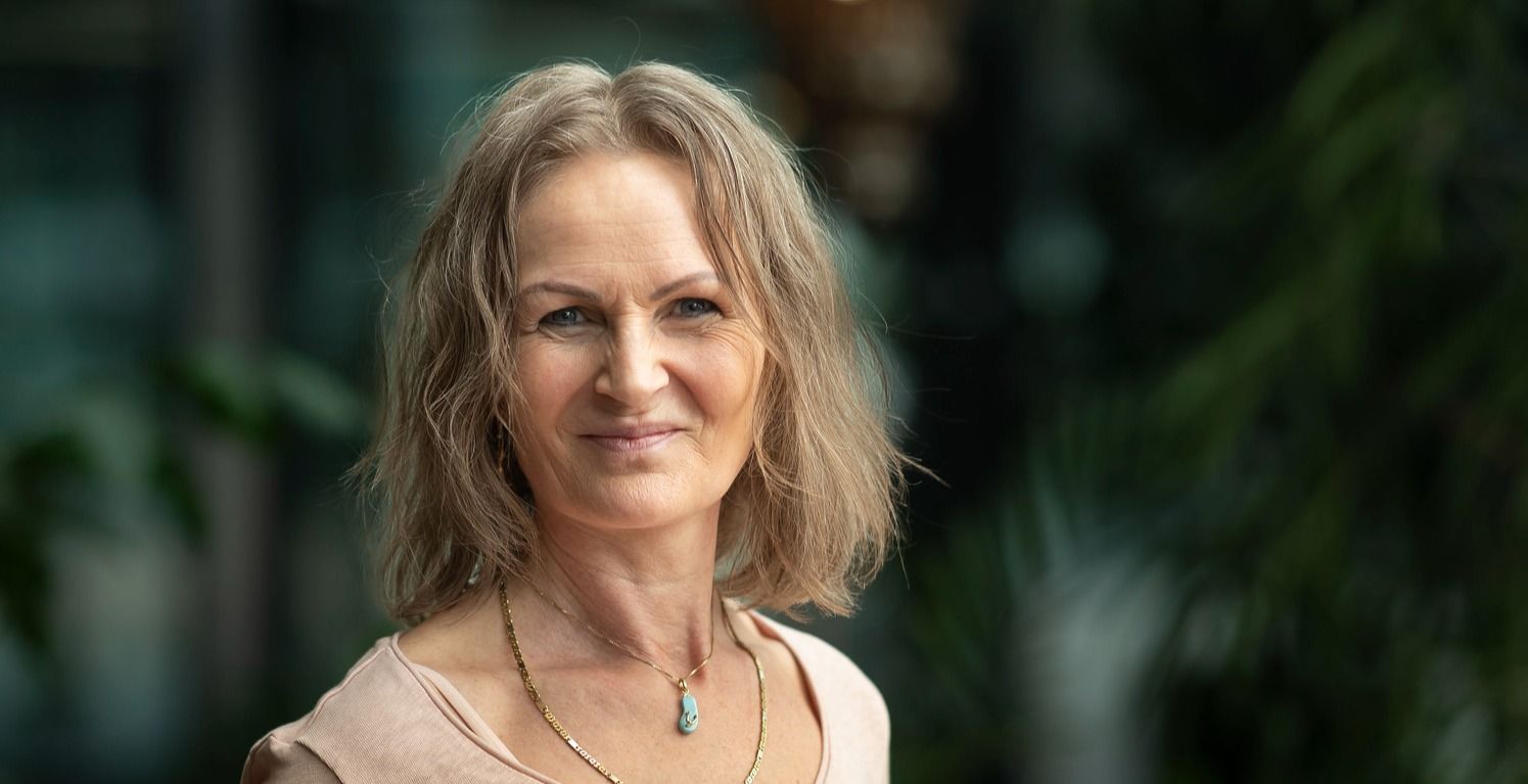 Person med blondt hår i beige genser, bakgrunn med grønne planter