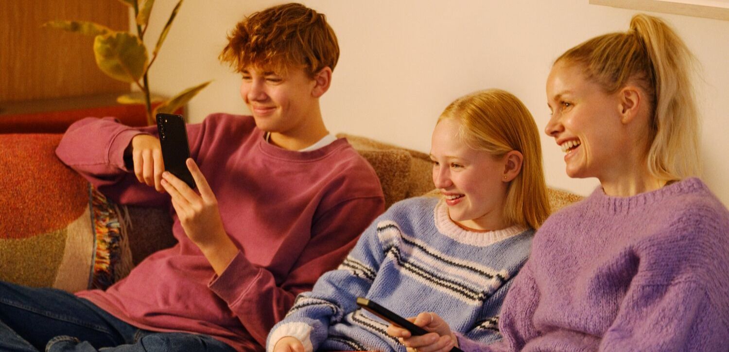 Tre personer på en sofa med mobiltelefoner og en rød bolle