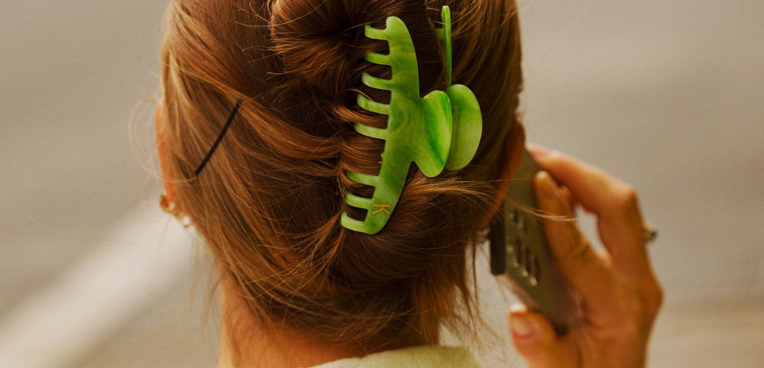 Kvinne med oppsatt hår og grønn hårklemme prater i telefon