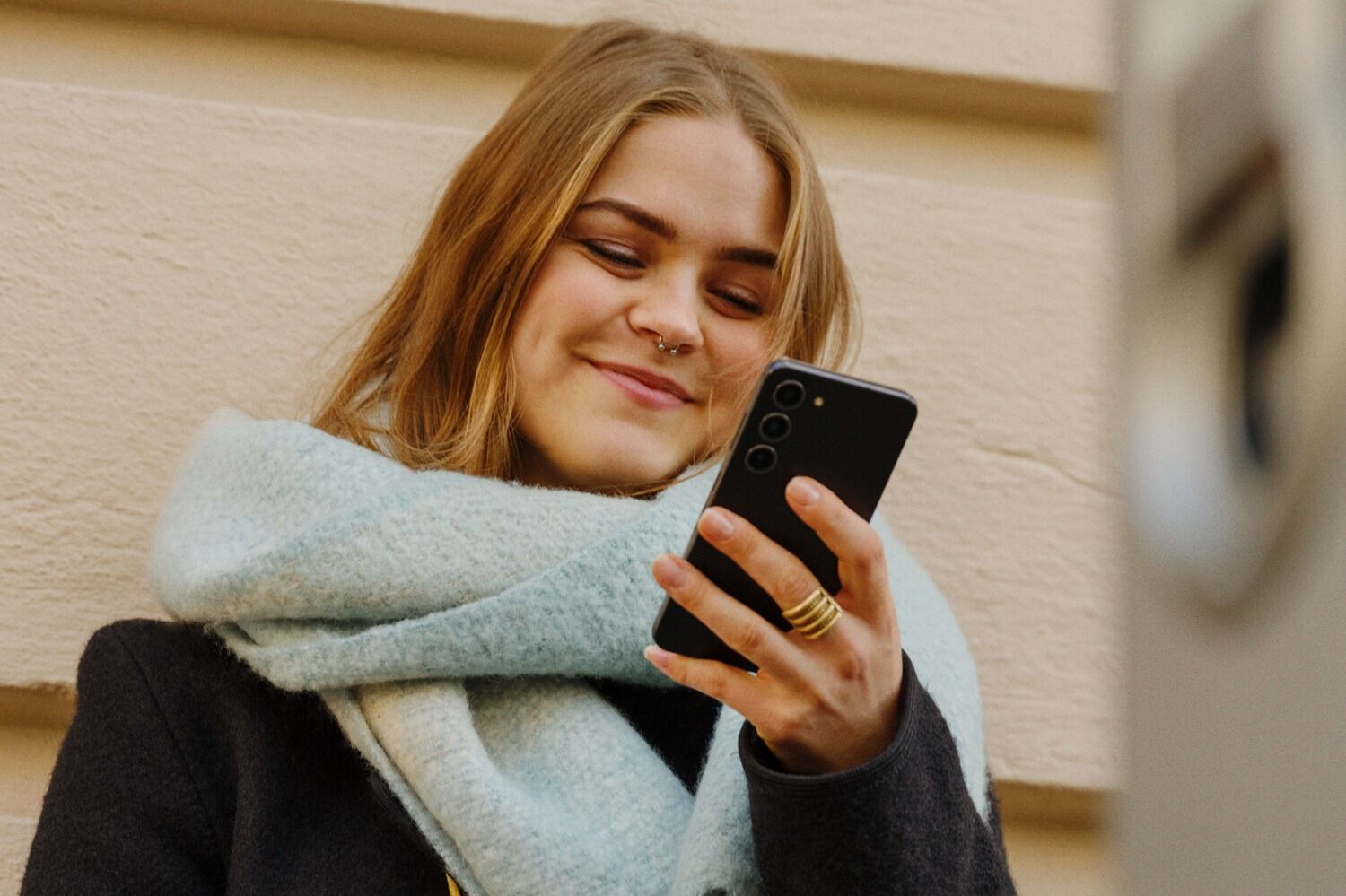 Person med svart frakk og lyseblått skjerf holder en mobiltelefon