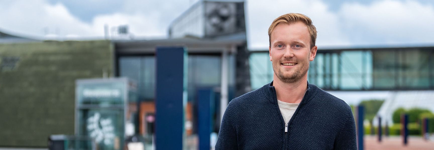 Mann i blå jakke og jeans foran bygning