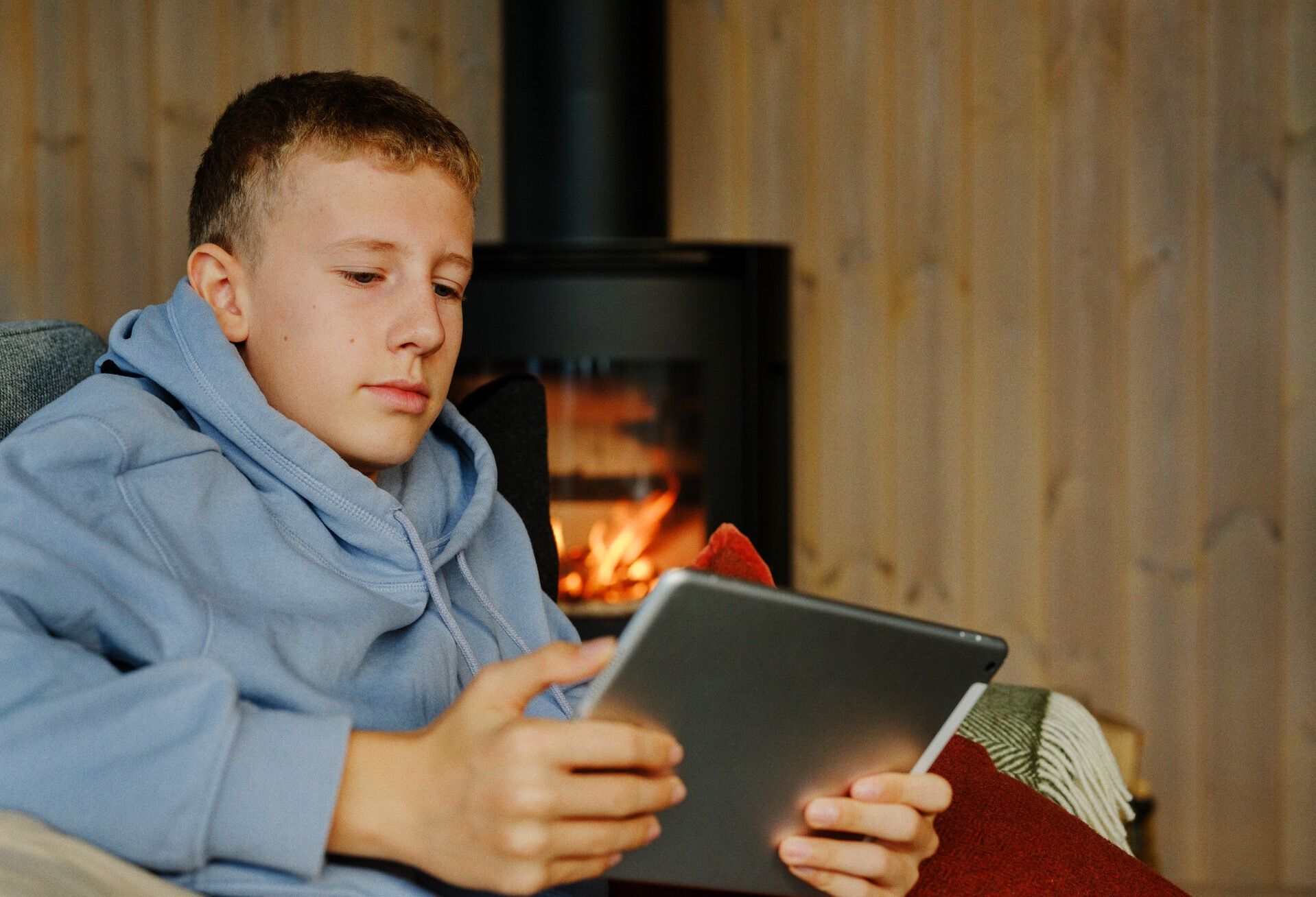 Person i blå hettegenser bruker et nettbrett foran en peis