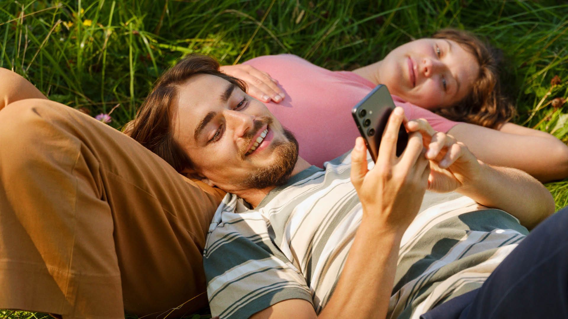 Gutt og jente i gresset som ser på bilder i Min Sky