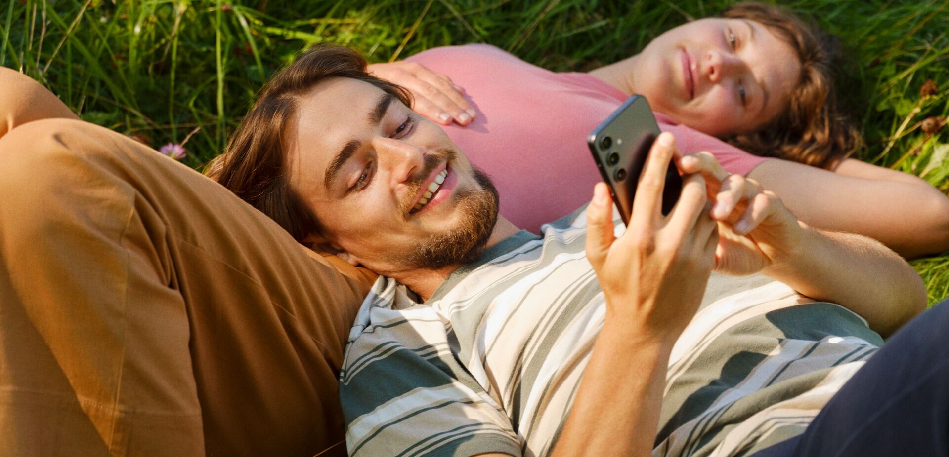 To ligger på gress og ser på telefon