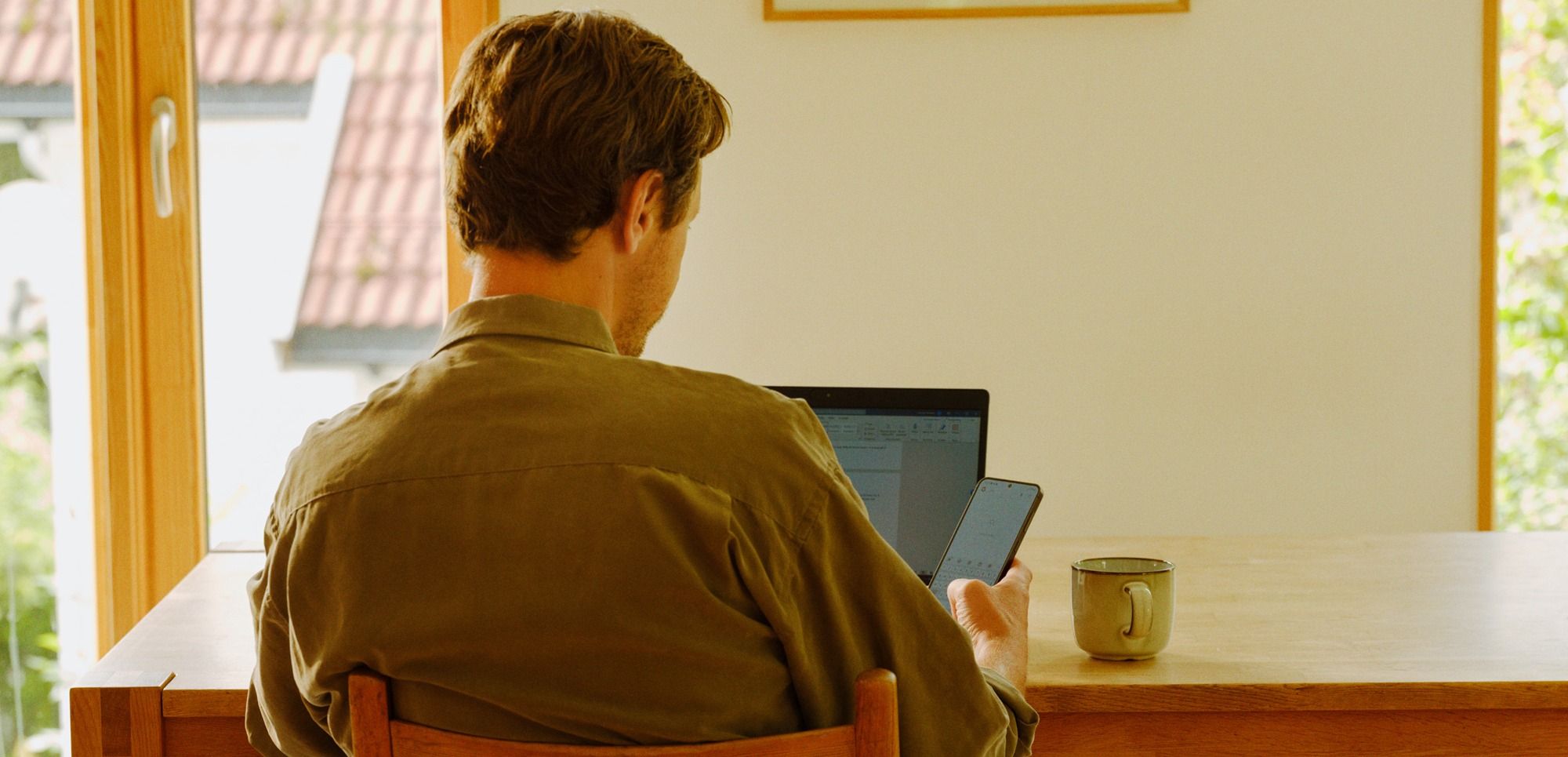 Person jobber ved et trebord med laptop og mobil og gjennomfører en sikkerhetssjekk