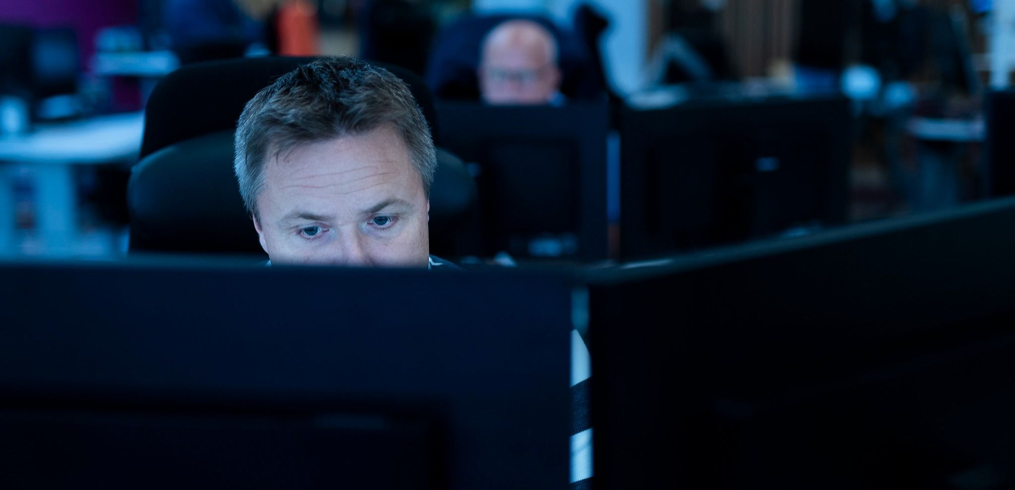 Kontorlandskap med flere dataskjermer og uklart bakgrunnsmiljø