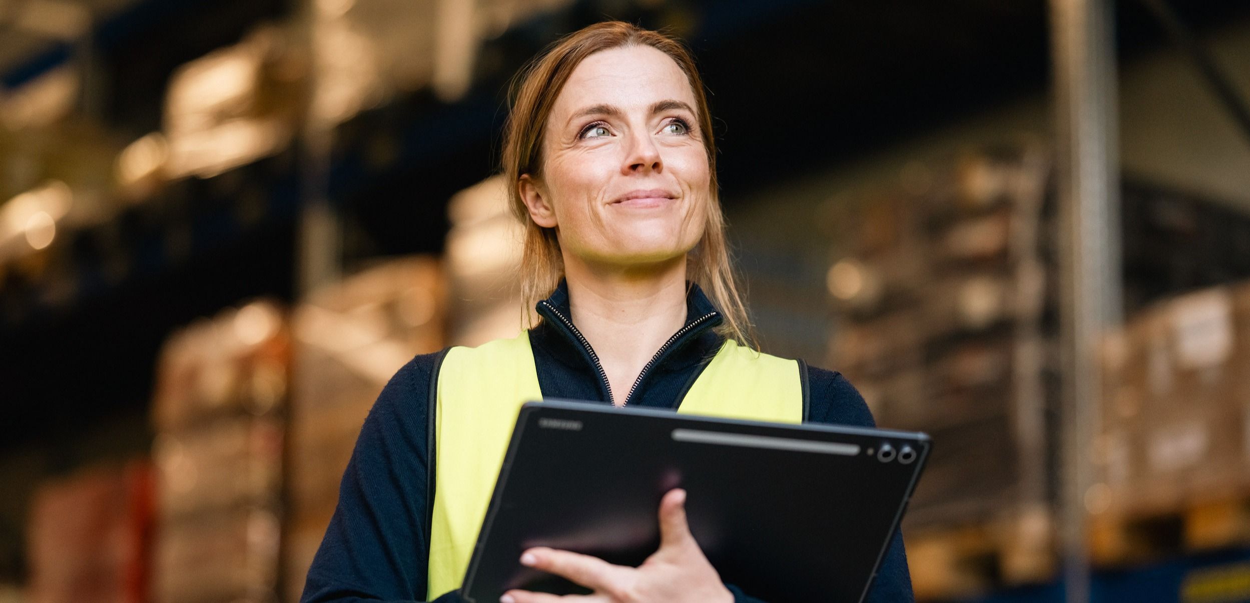 Kvinne i industrien med nettbrett og gul sikkerhetsvest koblet til mobilnett