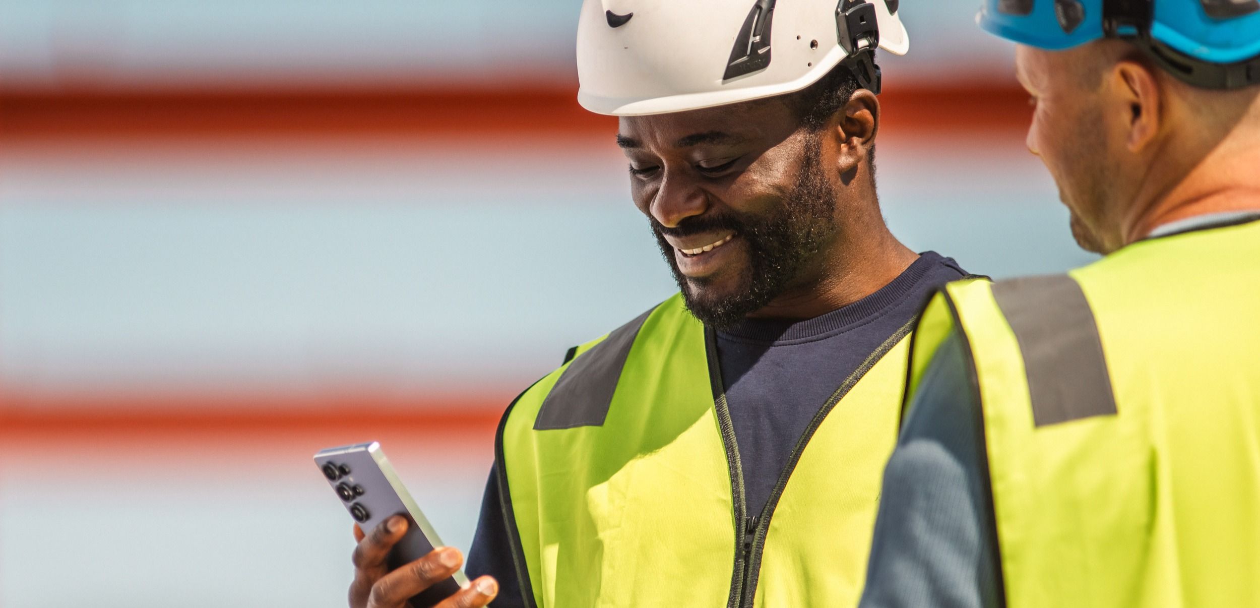 Industriarbeidere med vernehjelm og refleksvest ser på en mobil