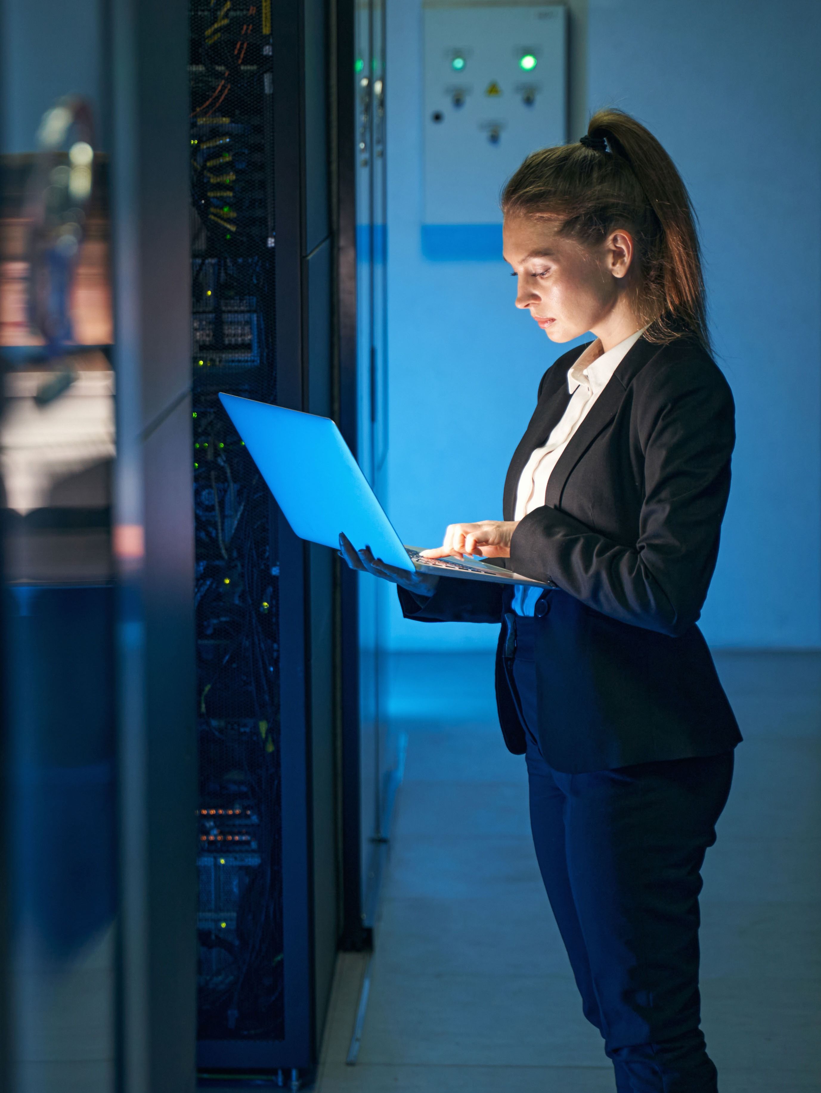Kvinne i dress jobber med en laptop i et serverrom