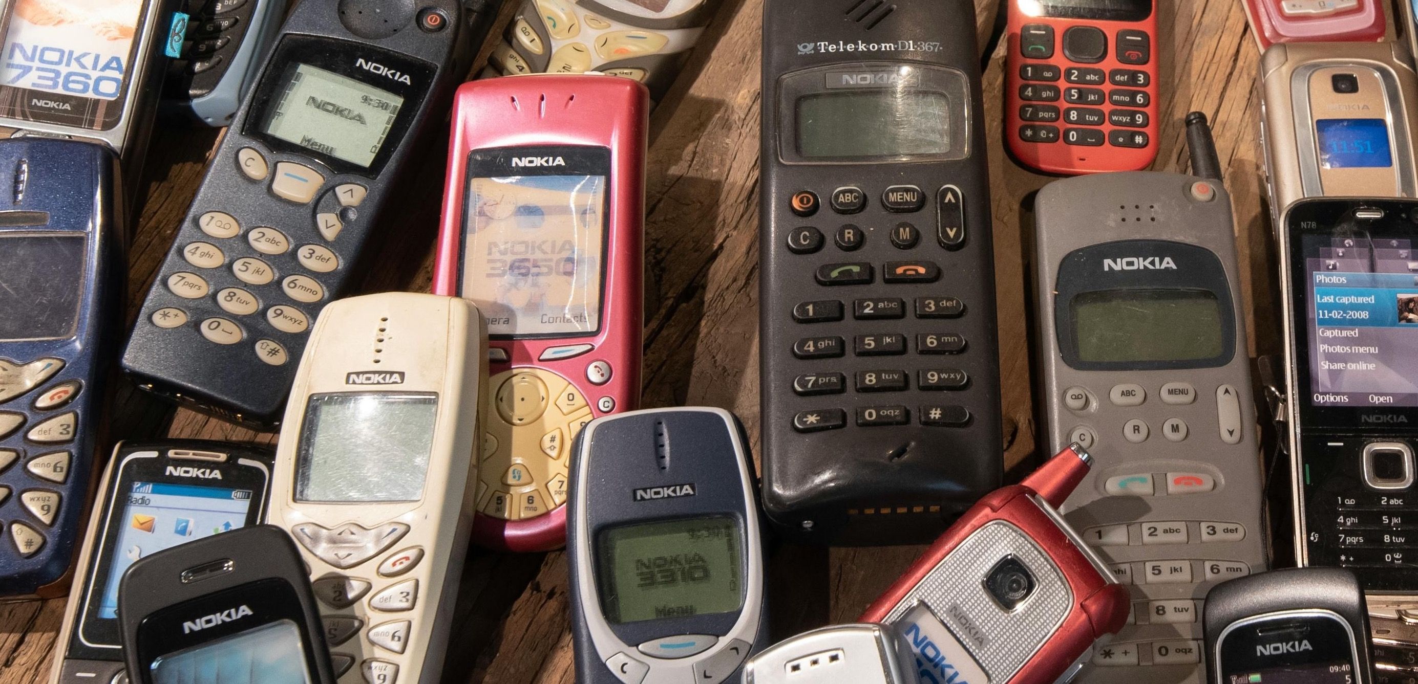 Flere gamle Nokia-mobiler ligger spredt på en treoverflate